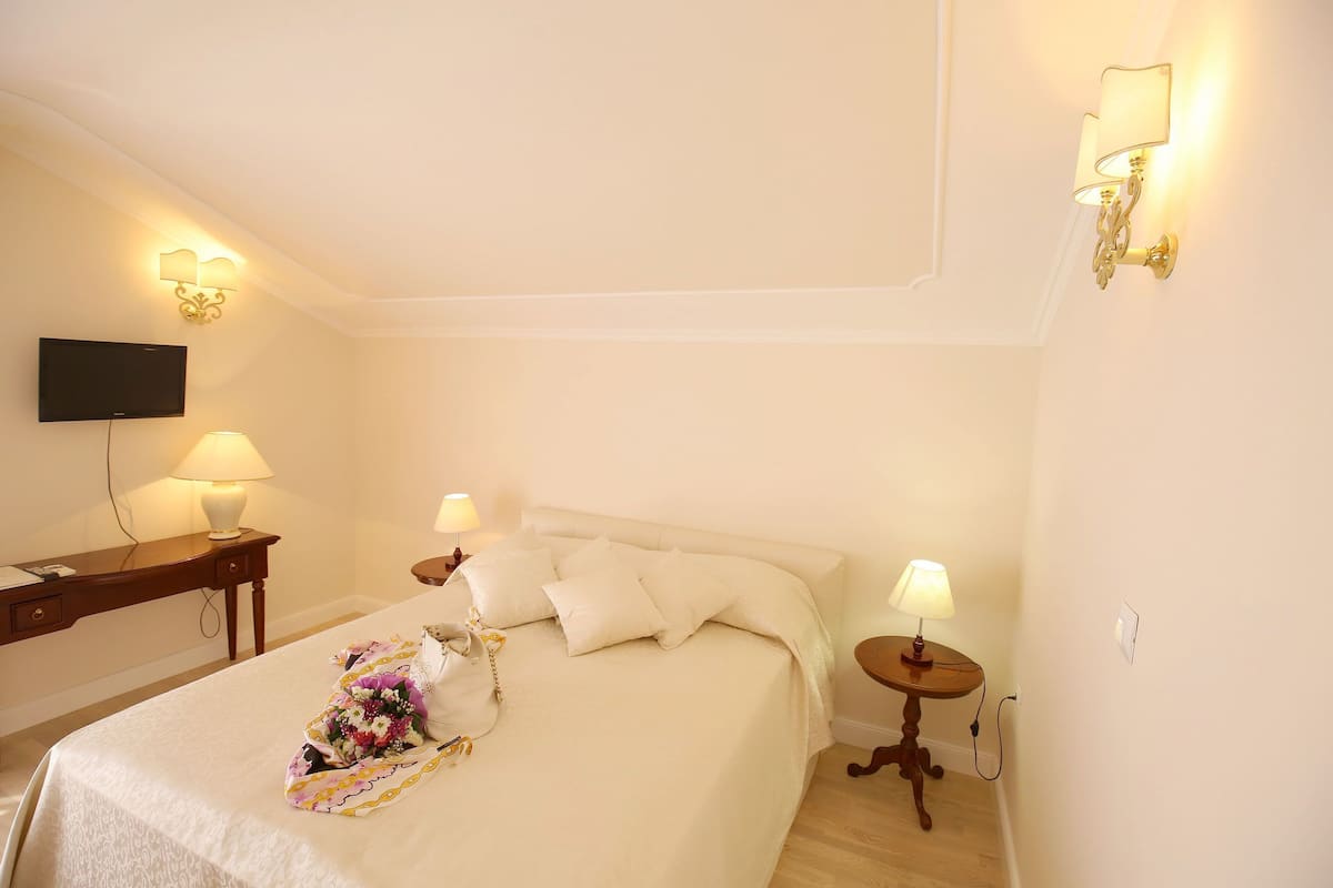 A hotel room with a bed, bedside lamps, a flat-screen TV, and a desk with a lamp.