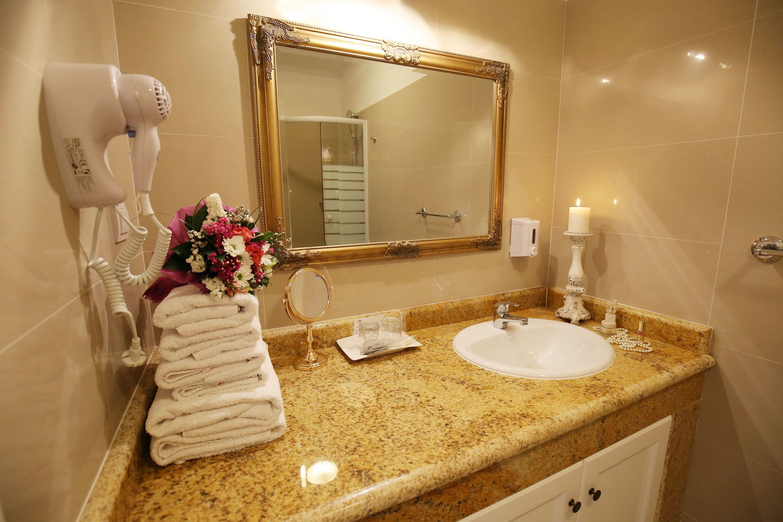 A bathroom with a marble countertop, a sink, a large mirror, a hairdryer, a towel rack, and a candle.
