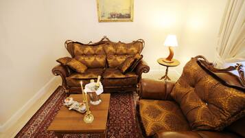 A living room with a brown patterned sofa, a wooden coffee table with a candle and a bottle, a patterned rug, and a small table with a lamp.