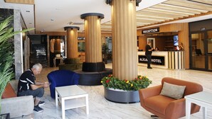 A hotel reception area with a reception desk, a seating area with sofas and a coffee table, and a large planter with flowers. - Alican Hotel (Izmir)