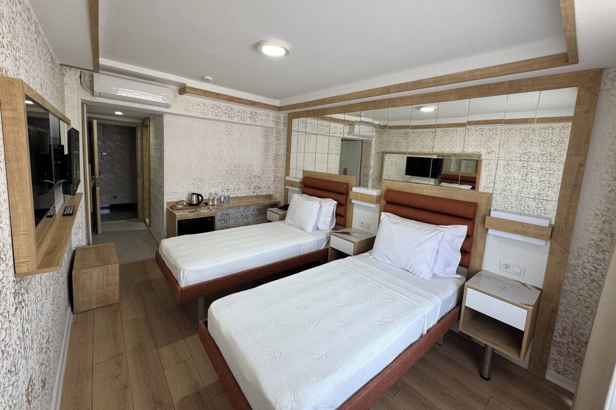 A hotel room with two beds, a small desk, a mirror, and a bathroom with a shower and toilet.