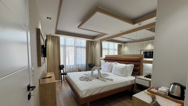 A modern hotel room with a large bed, a bedside table with a kettle, a microwave, and a small seating area with a chair and a table. - Alican Hotel (Izmir)