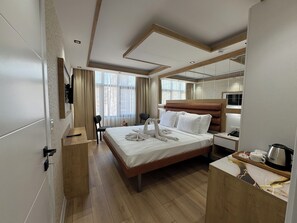 A modern hotel room with a large bed, a bedside table with a kettle, a microwave, and a small seating area with a chair and a table. - Alican Hotel (Izmir)