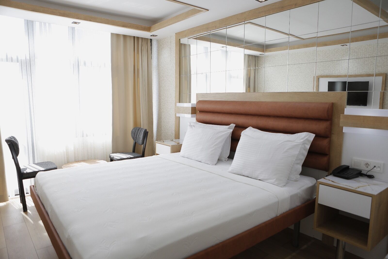 A hotel room with a large bed, a bedside table with a phone, and a chair.