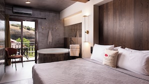 A modern hotel room with a large bed, a round bathtub, a balcony with a chair, and a view of the outdoors. - Tsikeli Boutique Hotel Meteora - Adults Friendly (Kalabaka)