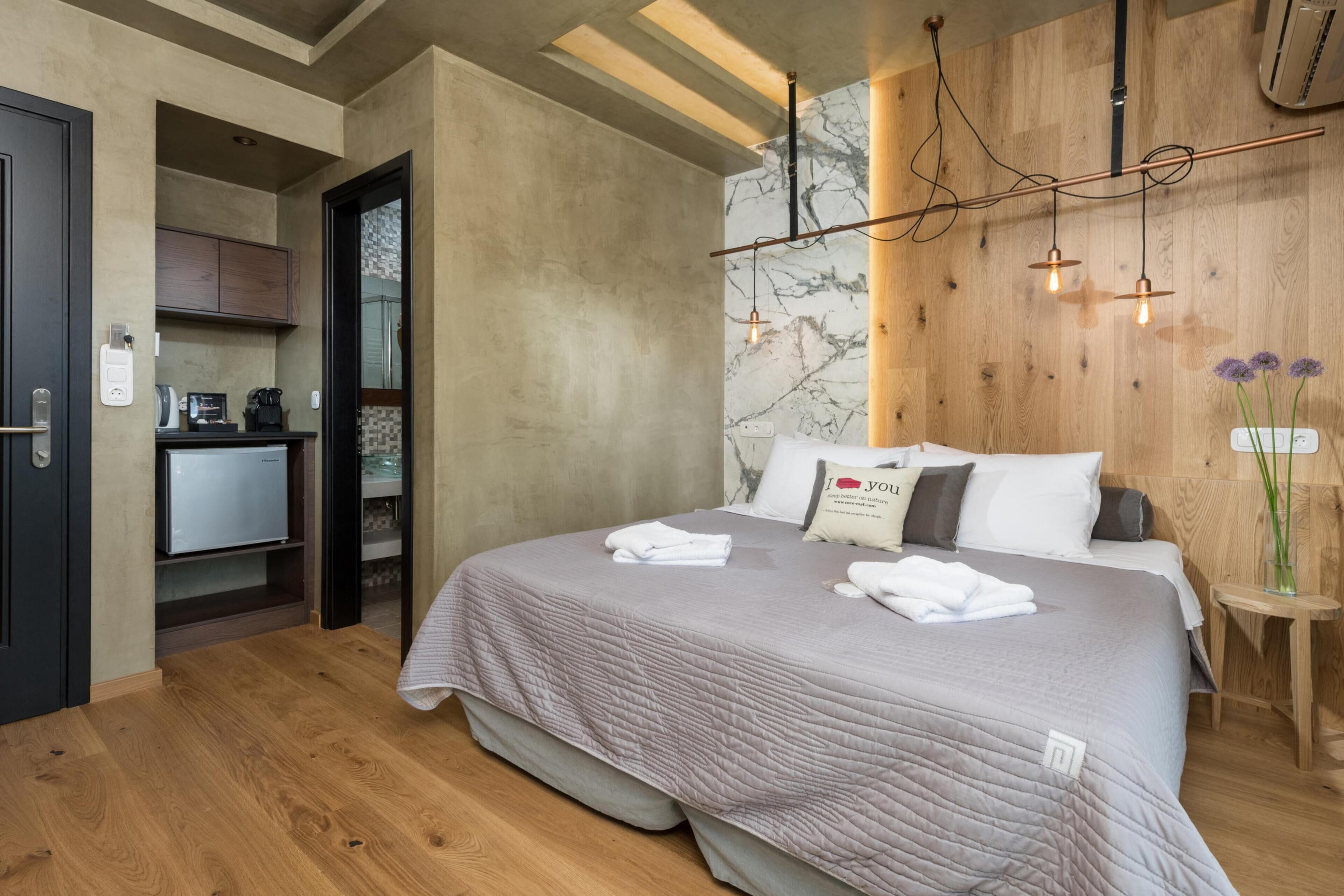 A modern hotel room with a bed, bedside table, and a small kitchenette.