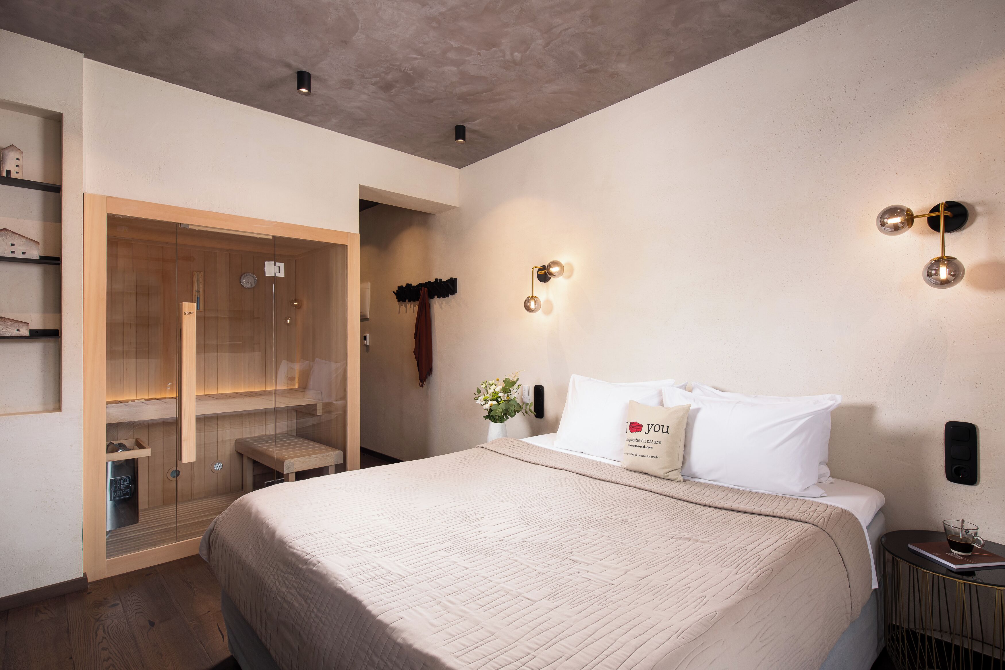 A modern hotel room with a large bed, a walk-in closet, and a bedside table with a lamp.
