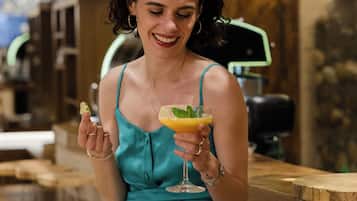A person seated at a bar with a drink in hand, glasses hanging above, and a bar counter.