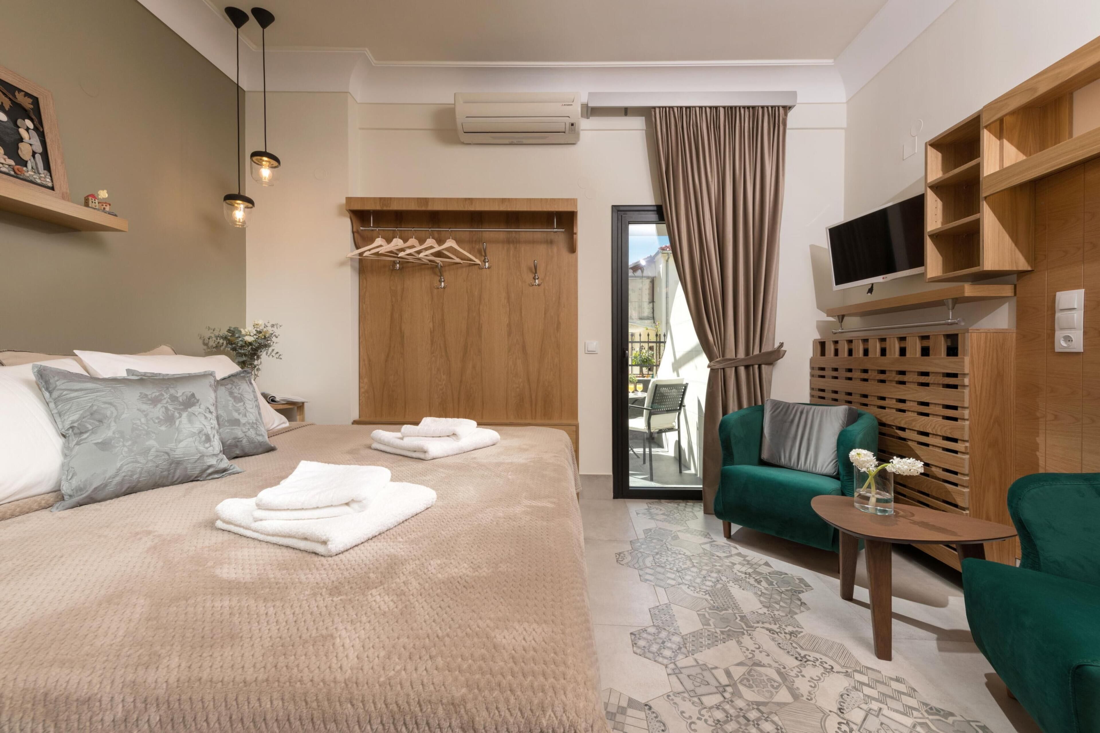 A modern hotel room with a large bed, a green sofa, a small table with a vase, and a TV mounted on a wooden shelf.