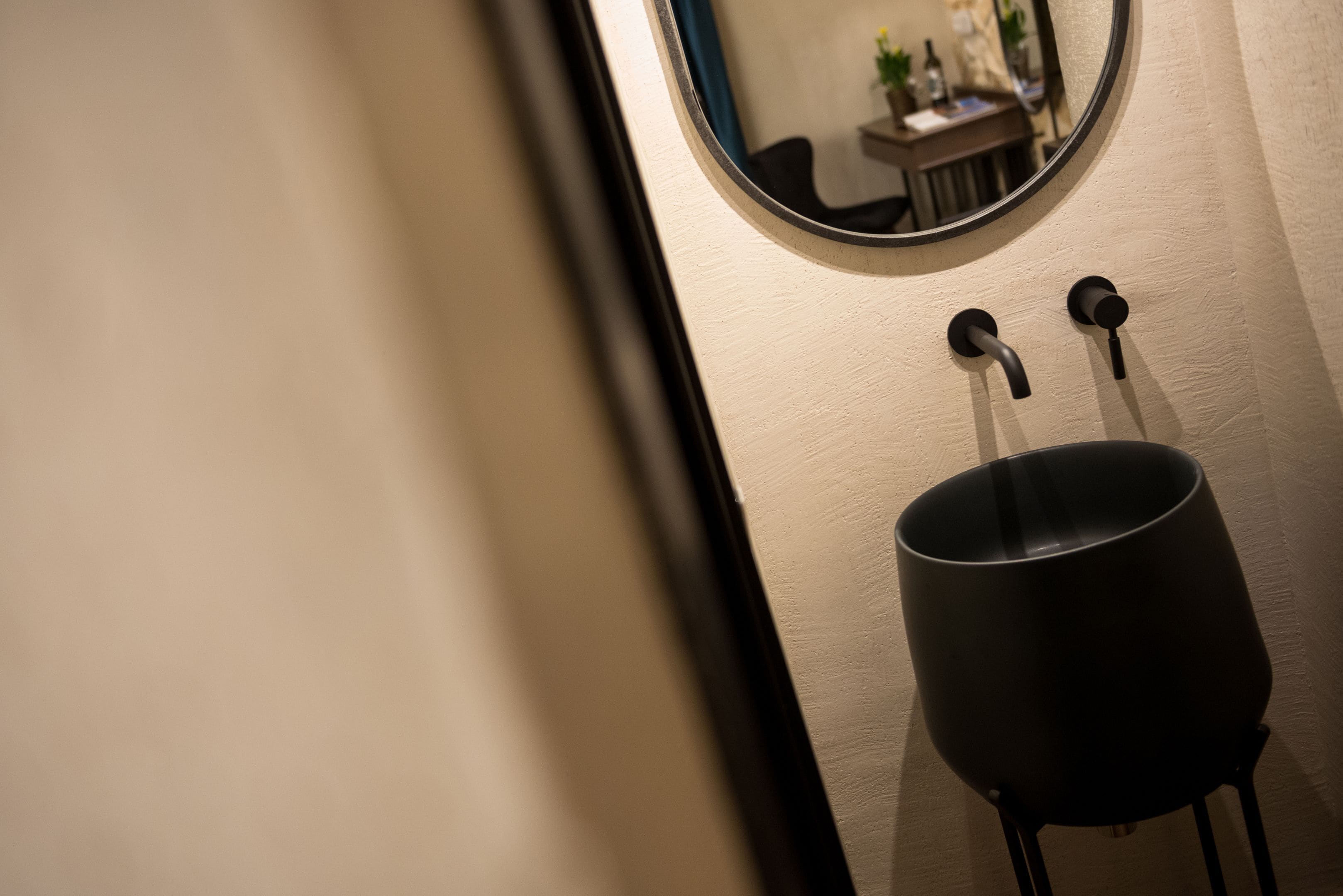 Un baño con un espejo redondo, un lavabo negro y un perchero para toallas.