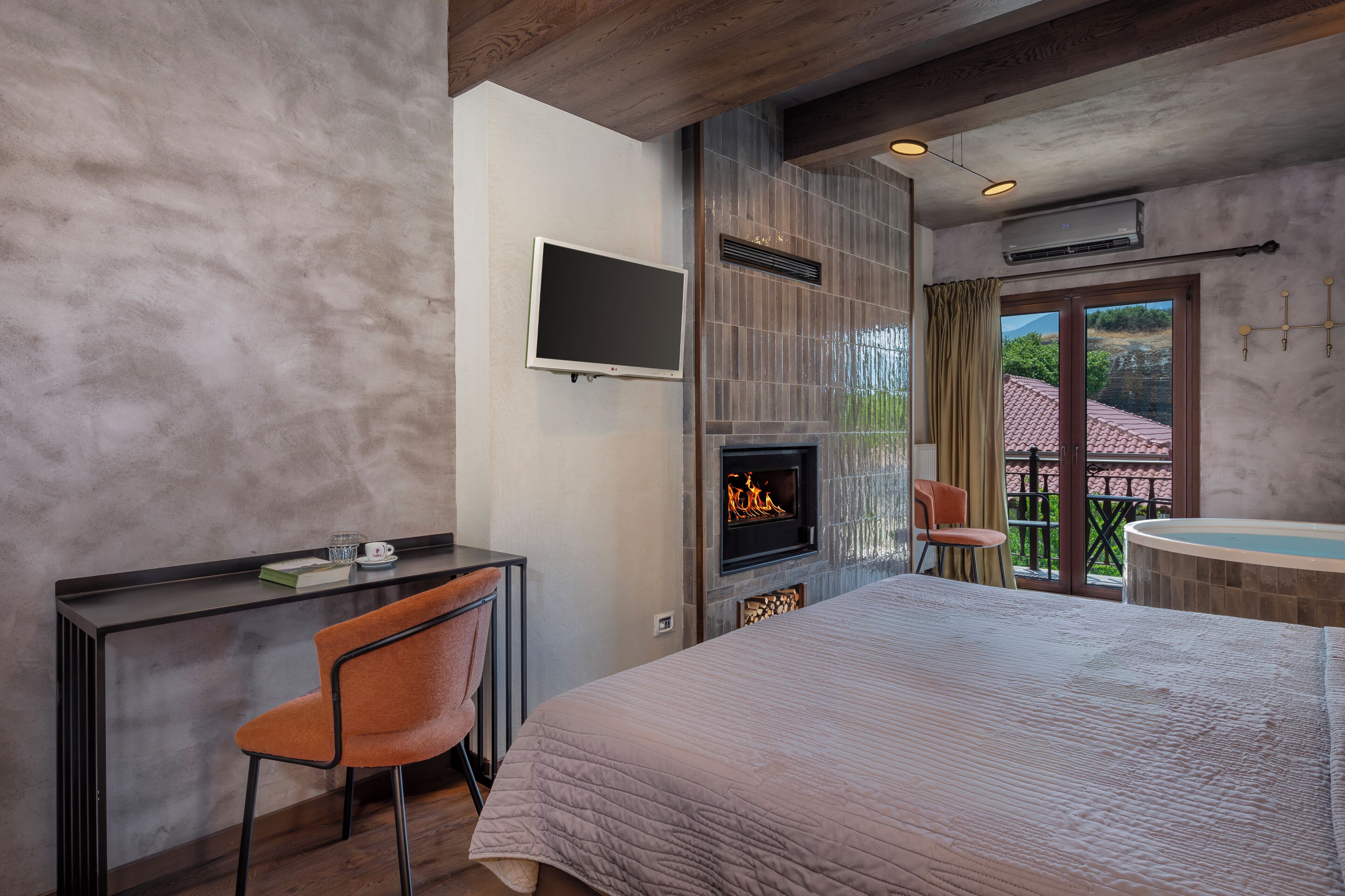 Un dormitorio con cama, escritorio y silla, chimenea, televisión y balcón con jacuzzi.
