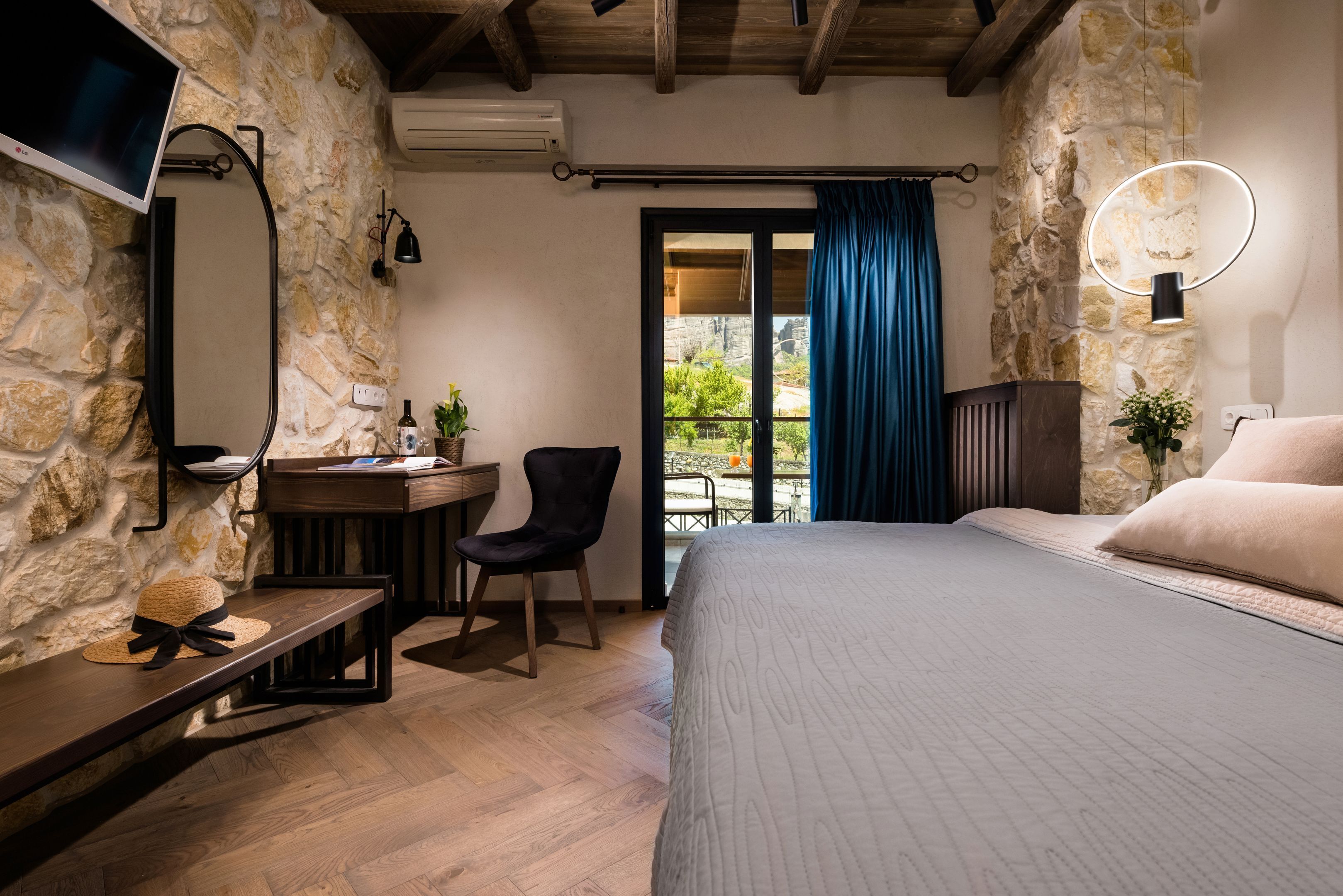 Ein Schlafzimmer mit Steinwand, Schreibtisch, Stuhl, Bett und Blick ins Freie.