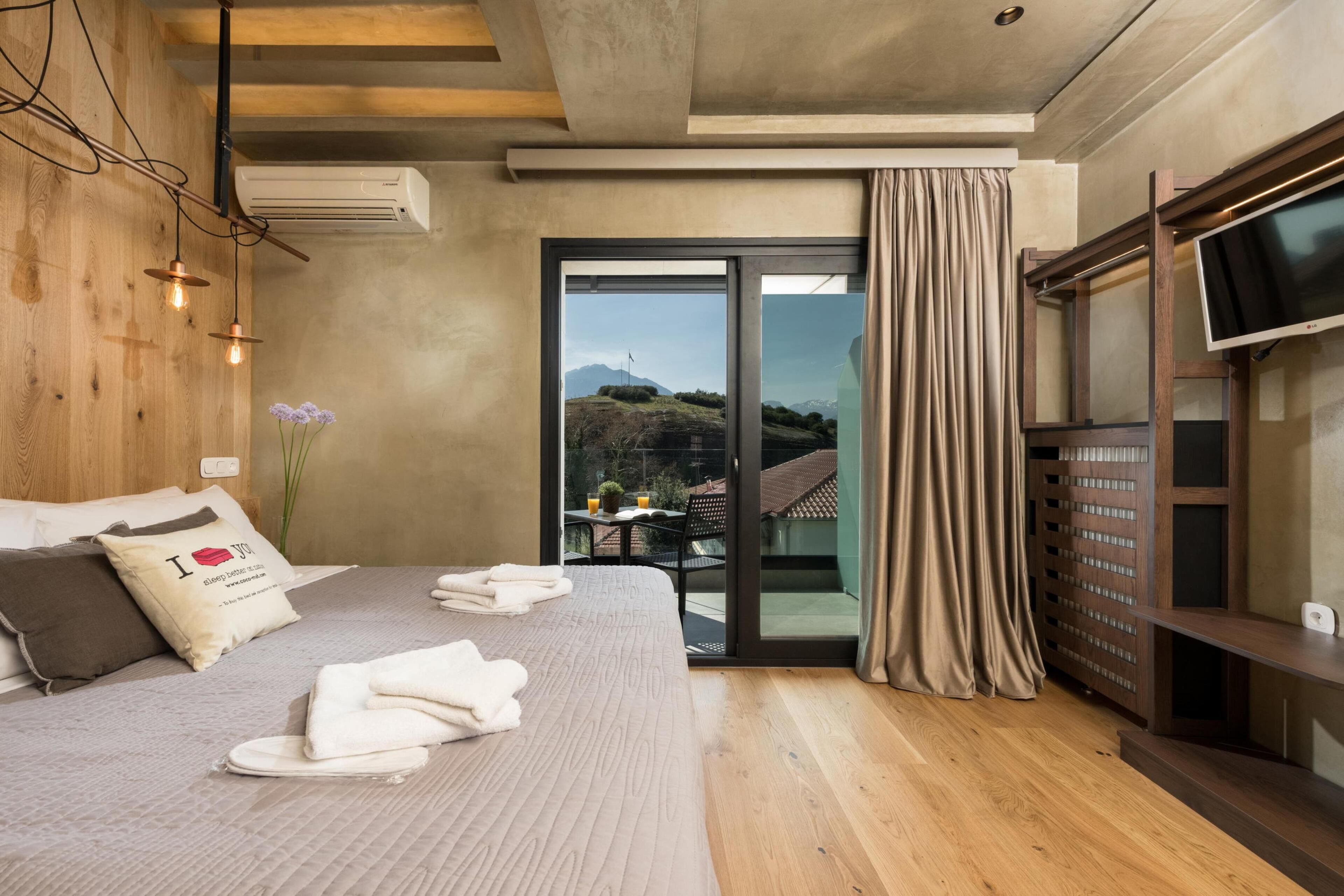 Una habitación de hotel moderna con una cama grande, una televisión de pantalla plana y una puerta corrediza de vidrio a un balcón.