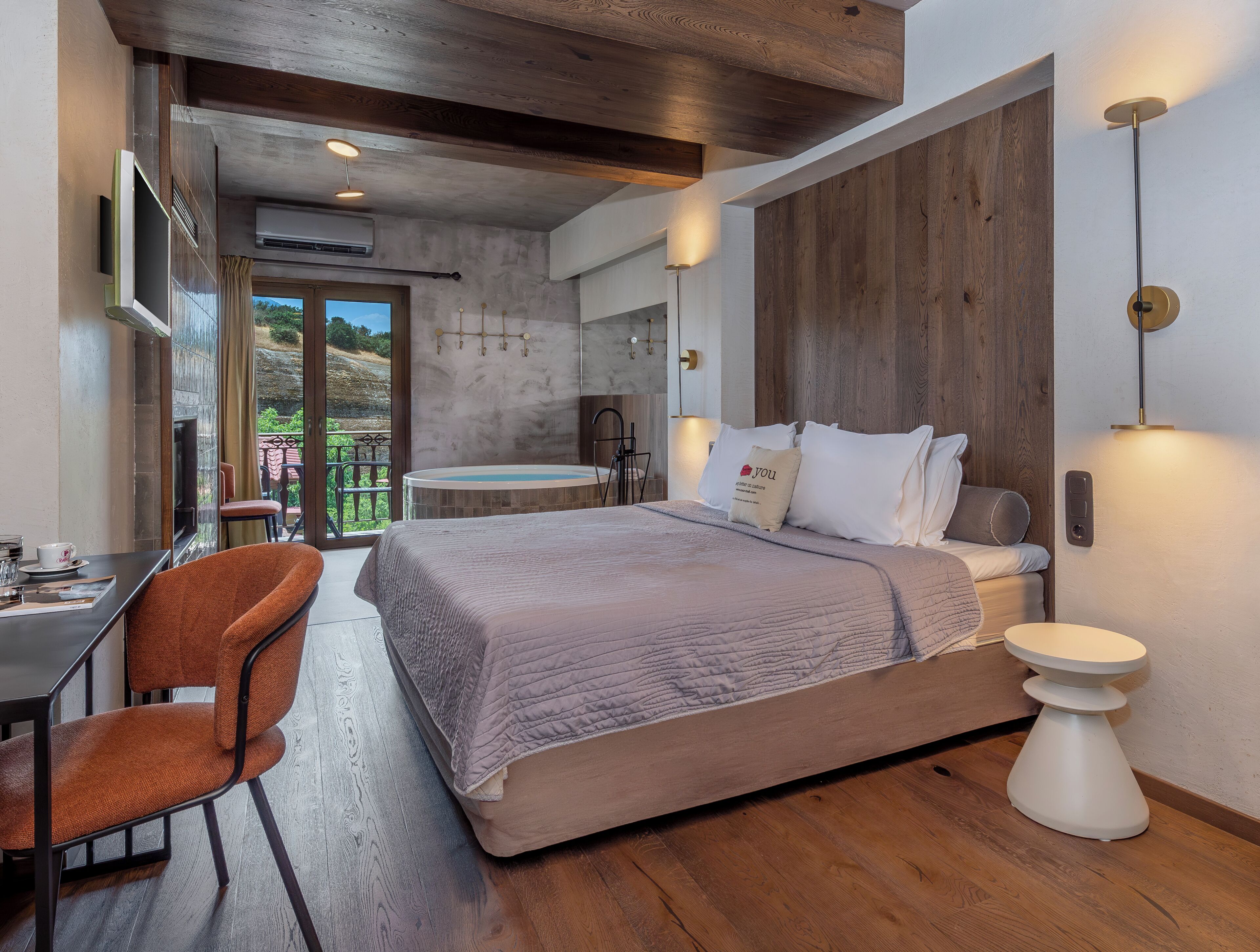 A modern bedroom with a large bed, a desk, and a view of the outdoors.