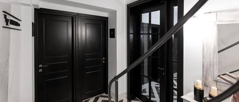 A hallway with black doors, a marble floor, and a staircase with a handrail.