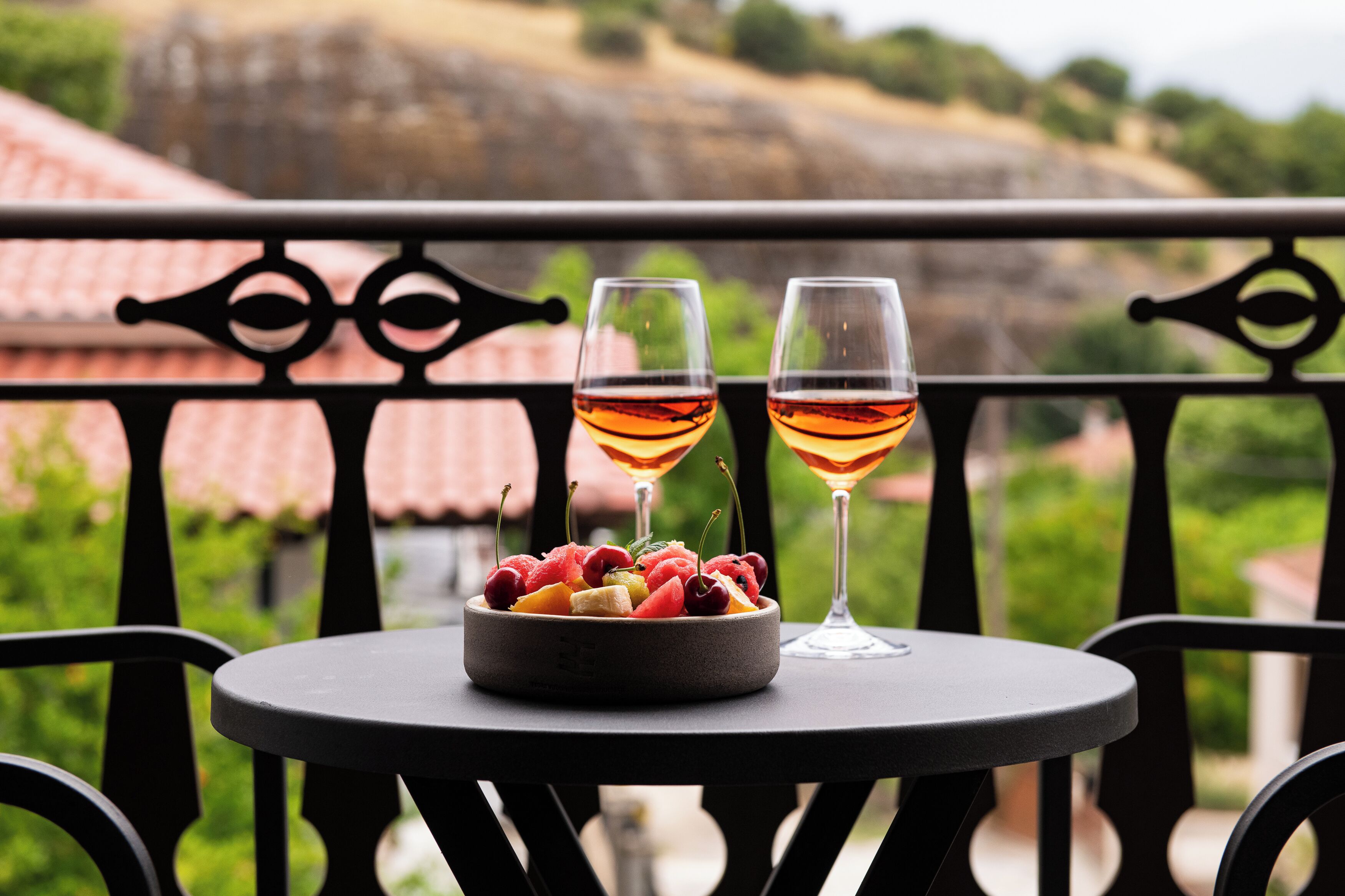 Ein Tisch mit Obstschale und zwei Gläsern Rotwein auf einem Balkon mit Blick auf einen Weinberg.