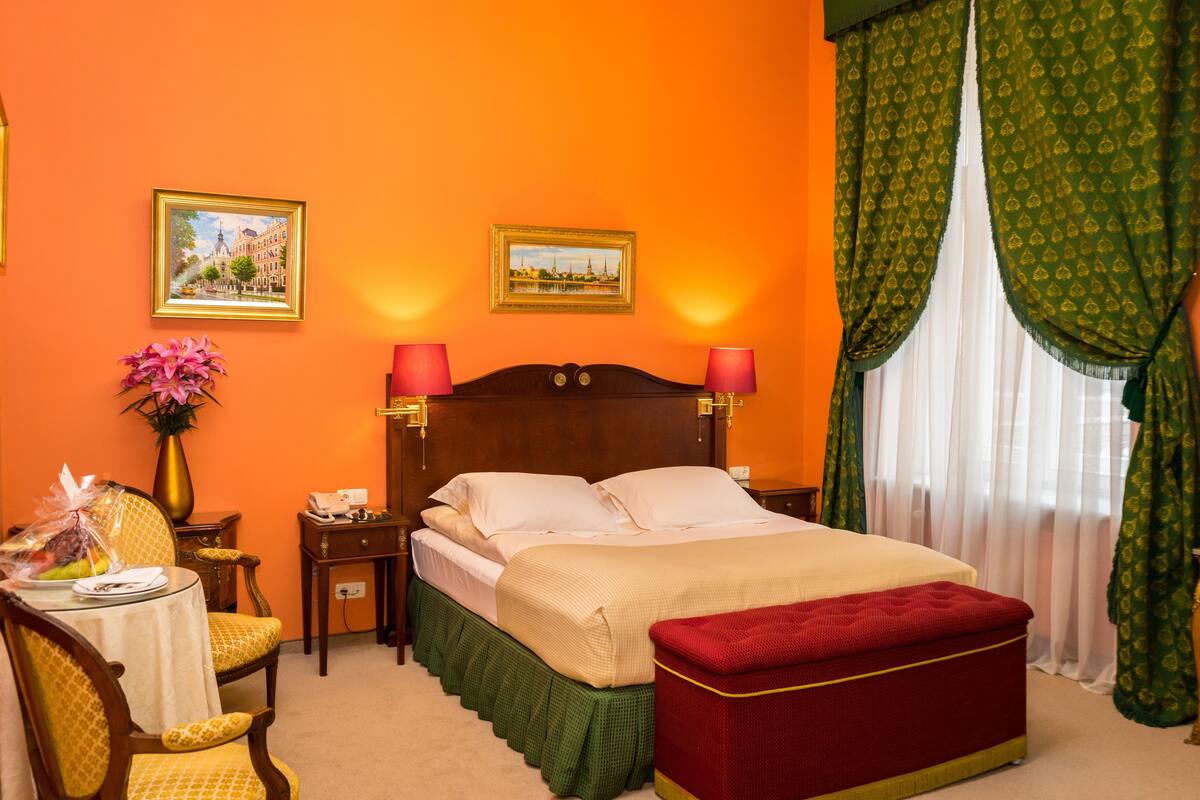 A hotel room with a bed, two bedside tables, a chair, a small table with a vase of flowers, and two framed pictures on the wall.