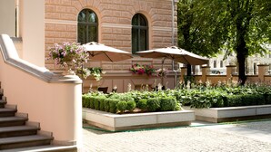 A building with a stone facade, outdoor seating with umbrellas, and a well-maintained garden. - Gallery Park Hotel & SPA, a Châteaux & Hôtels Collection (Riga)