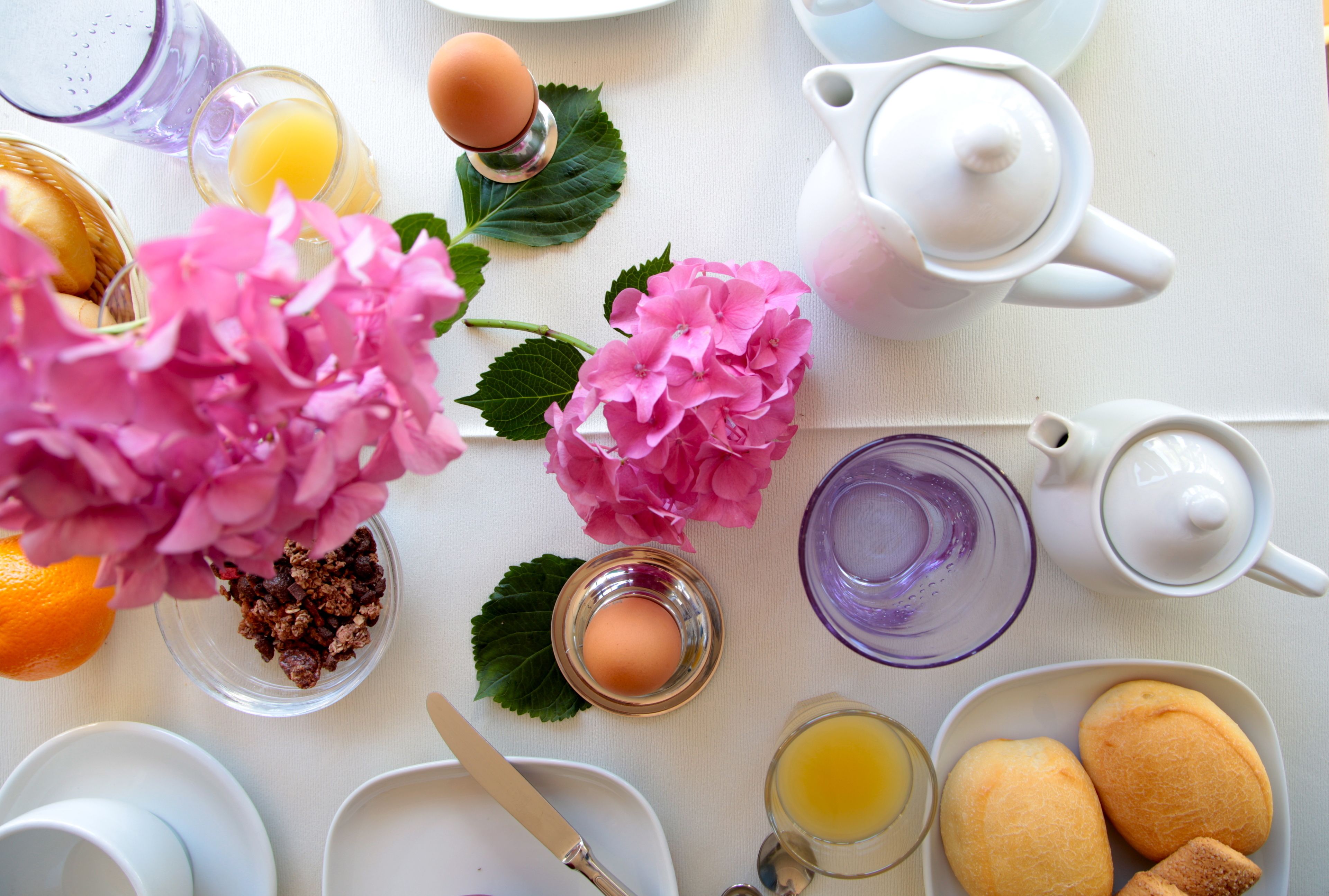 Una escena de desayuno con una mesa, platos, tazas, una tetera, una jarra y flores.