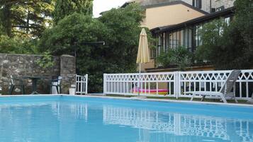 Relax by the serene pool surrounded by lush greenery and a stone building in the background.