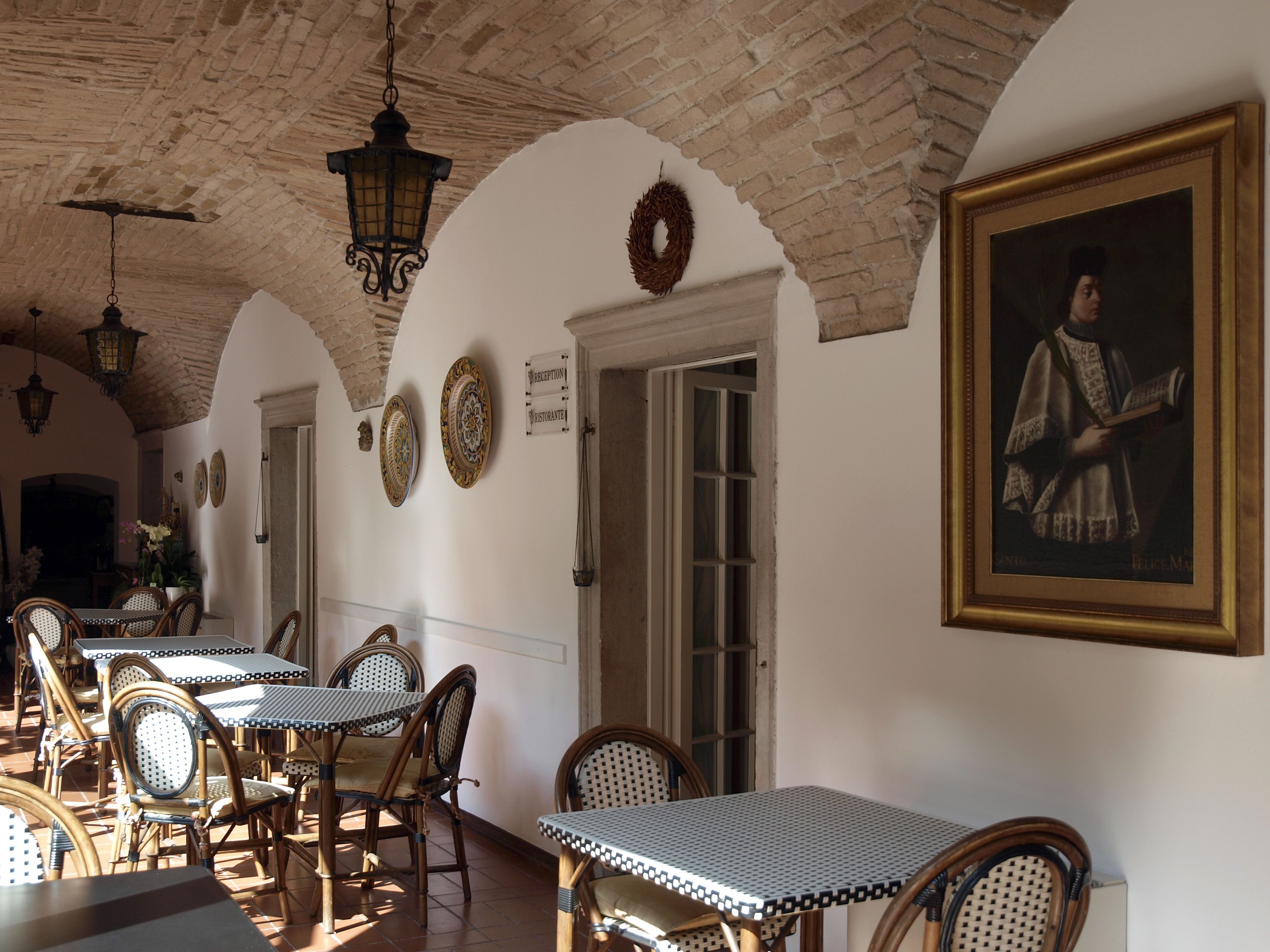 Un restaurante con arcos de ladrillo, mobiliario de mimbre y un retrato enmarcado en la pared.
