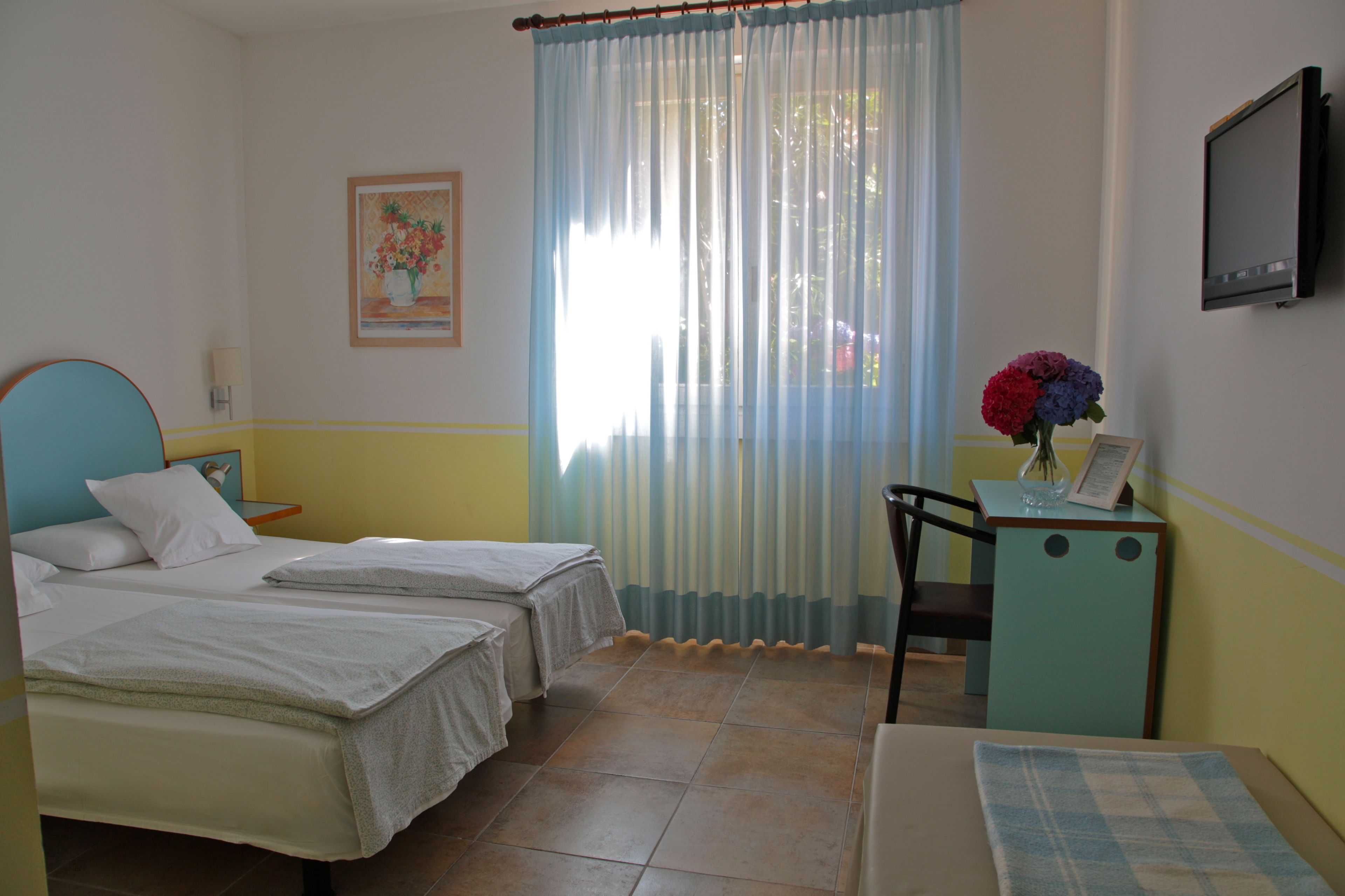 A hotel room with two beds, a desk with a chair, a television, and a window with curtains.