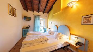 Una camera d'albergo con soffitto in legno, un letto con lenzuola bianche, un comodino con una lampada e una TV su un mobile.