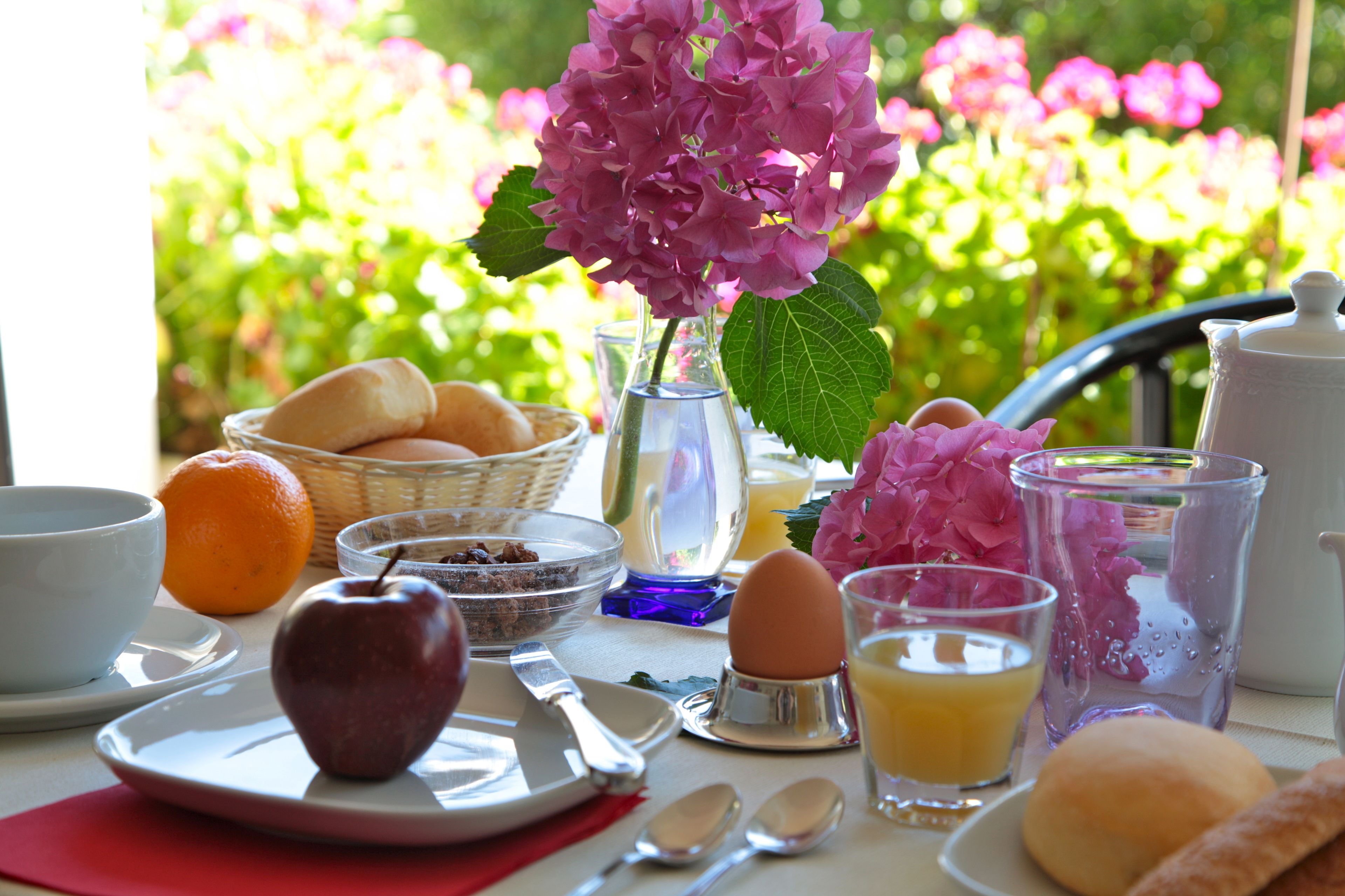 A breakfast table with a plate of food, a vase of flowers, and a teapot.