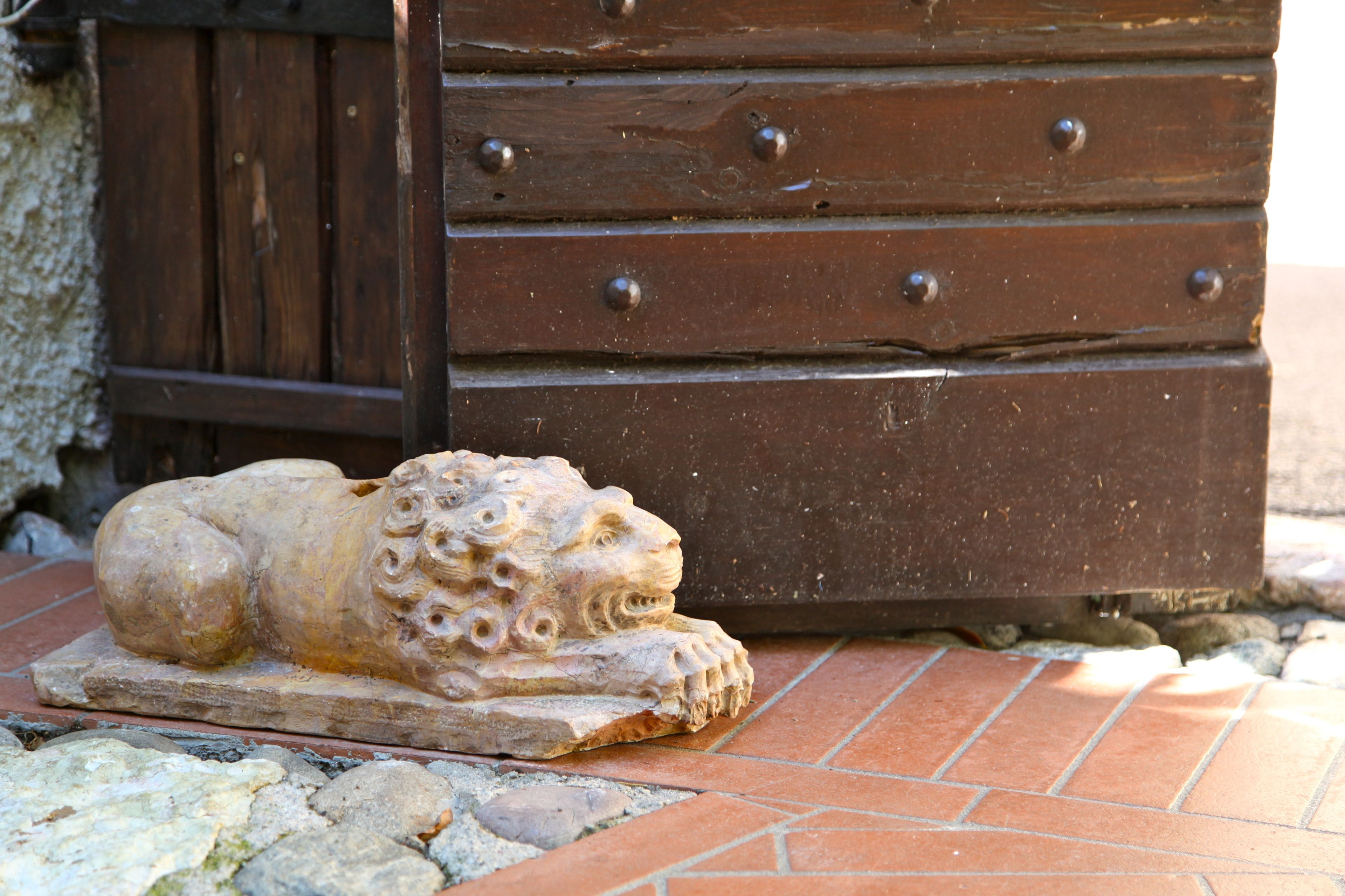 A stone lion statue on a brick platform, wooden dresser with metal knobs, and a stone wall in the background.