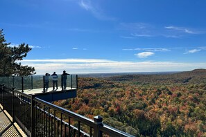A glass observation deck with a metal railing overlooking a forested valley. - Auberge de la Montagne Coupée (Saint-Jean-de-Matha)