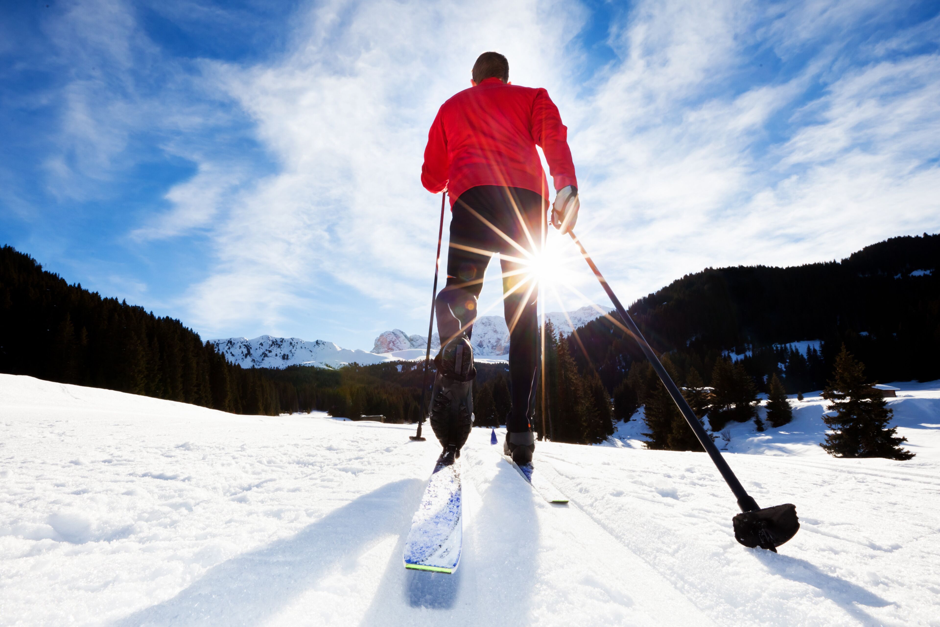 Eine Person fährt auf einem verschneiten Hang, der Himmel ist klar und im Hintergrund sind Berge zu sehen.