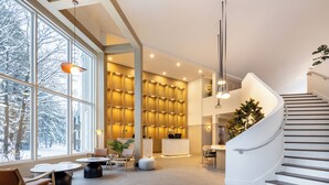 A modern hotel lobby with large windows, a reception desk, seating area, and a spiral staircase.