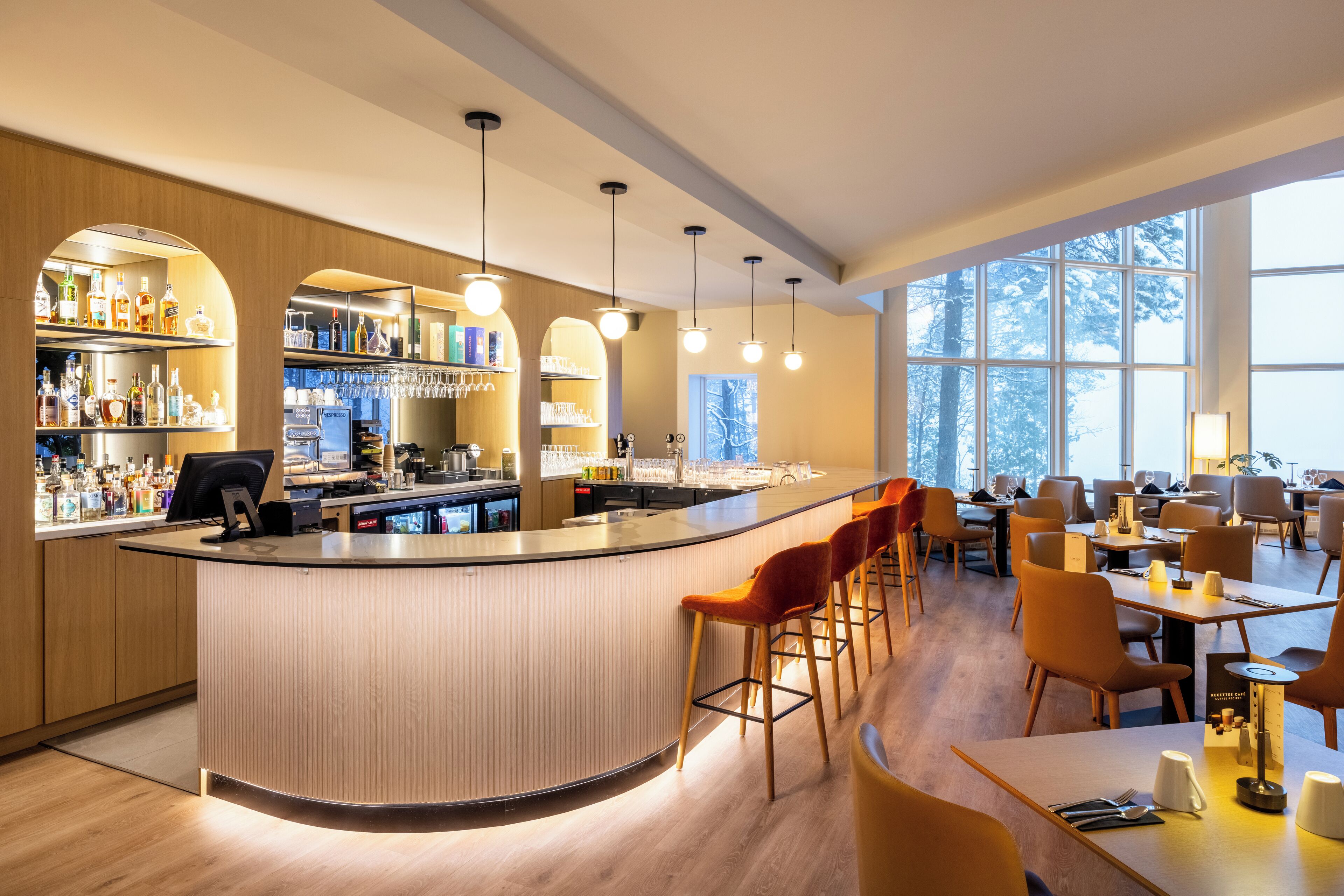 A modern bar area with a curved counter, bar stools, and a variety of liquor bottles.