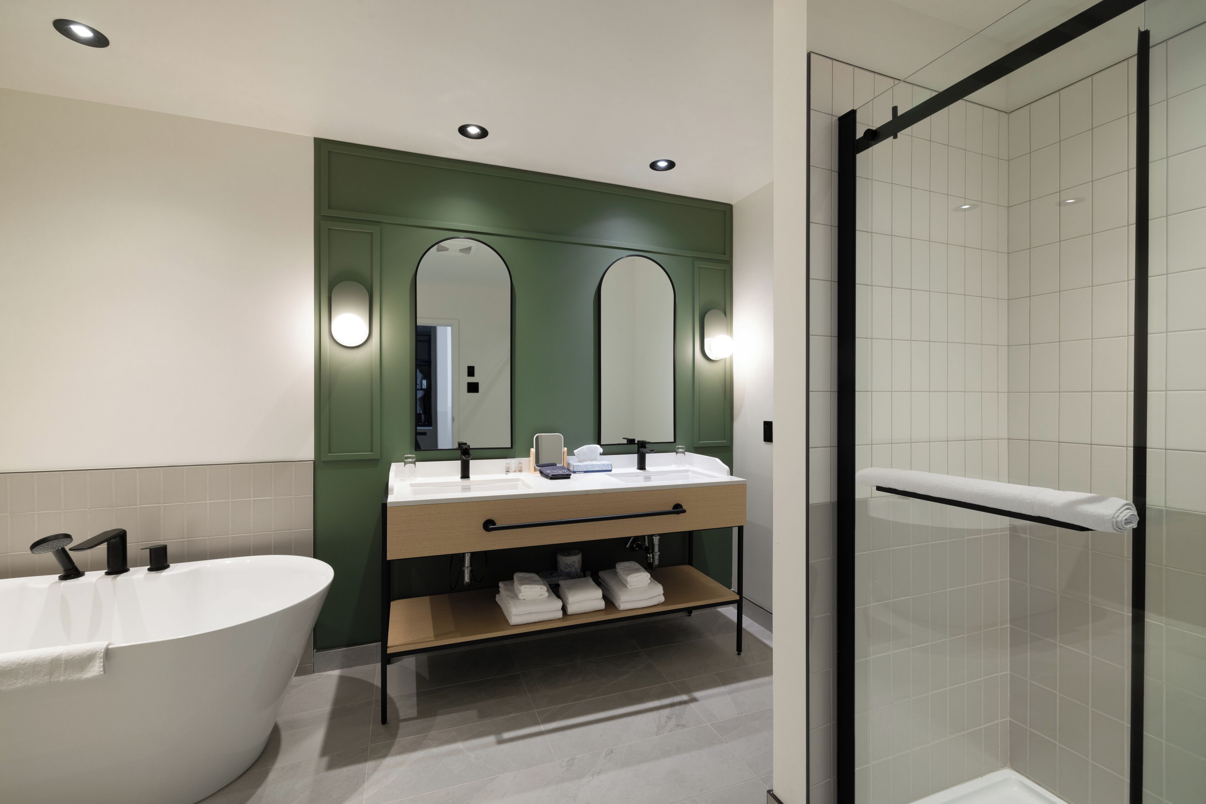 Een moderne badkamer met een vrijstaand bad, dubbele wastafels en een douche met glazen wanden.