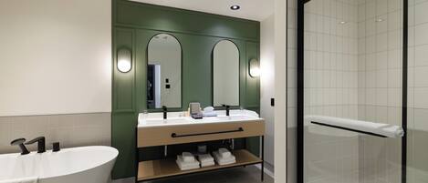 Een moderne badkamer met een vrijstaand bad, dubbele wastafels en een douche met glazen wanden.