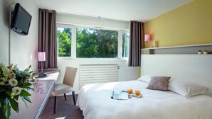 Habitación de hotel con cama, escritorio, silla, televisor, ventana con cortinas y mesita de noche con un tray con jugo de naranja.