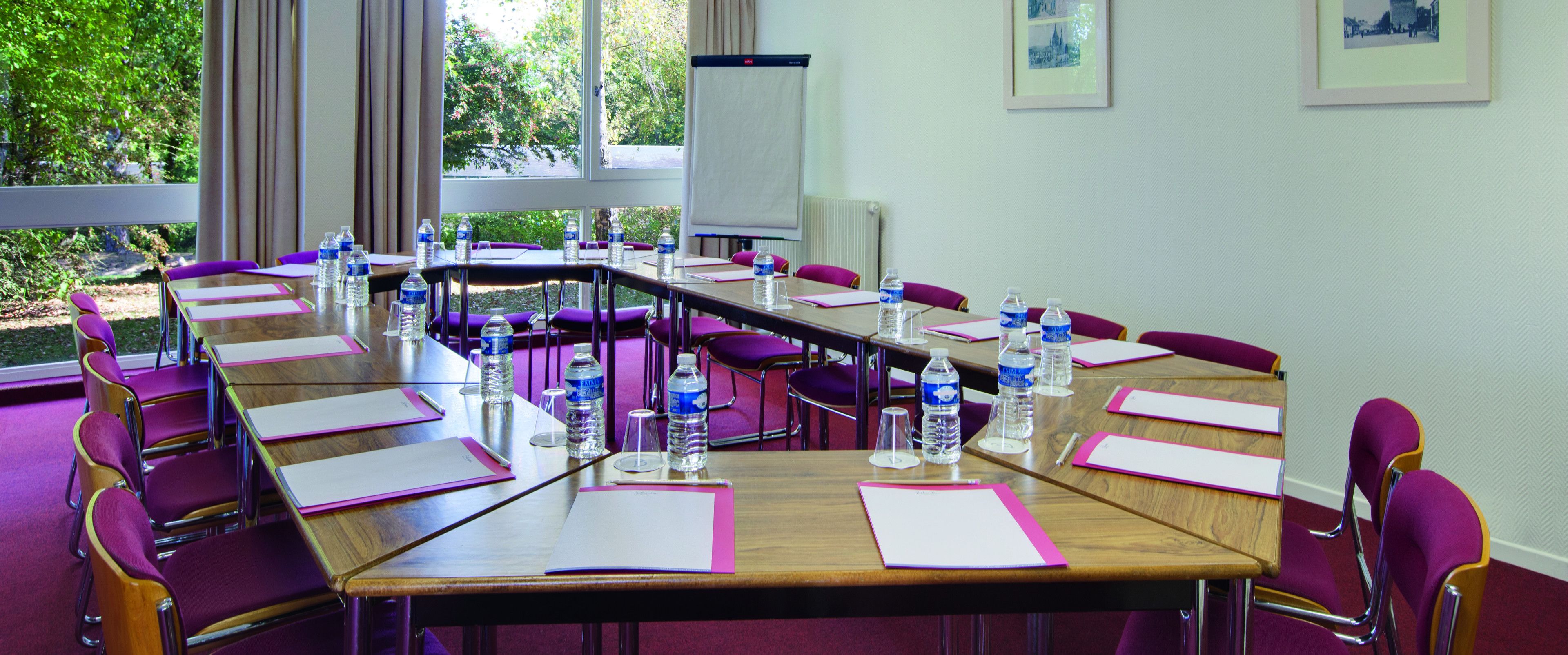 A conference room with a long table, purple chairs, water bottles, and a projector screen.