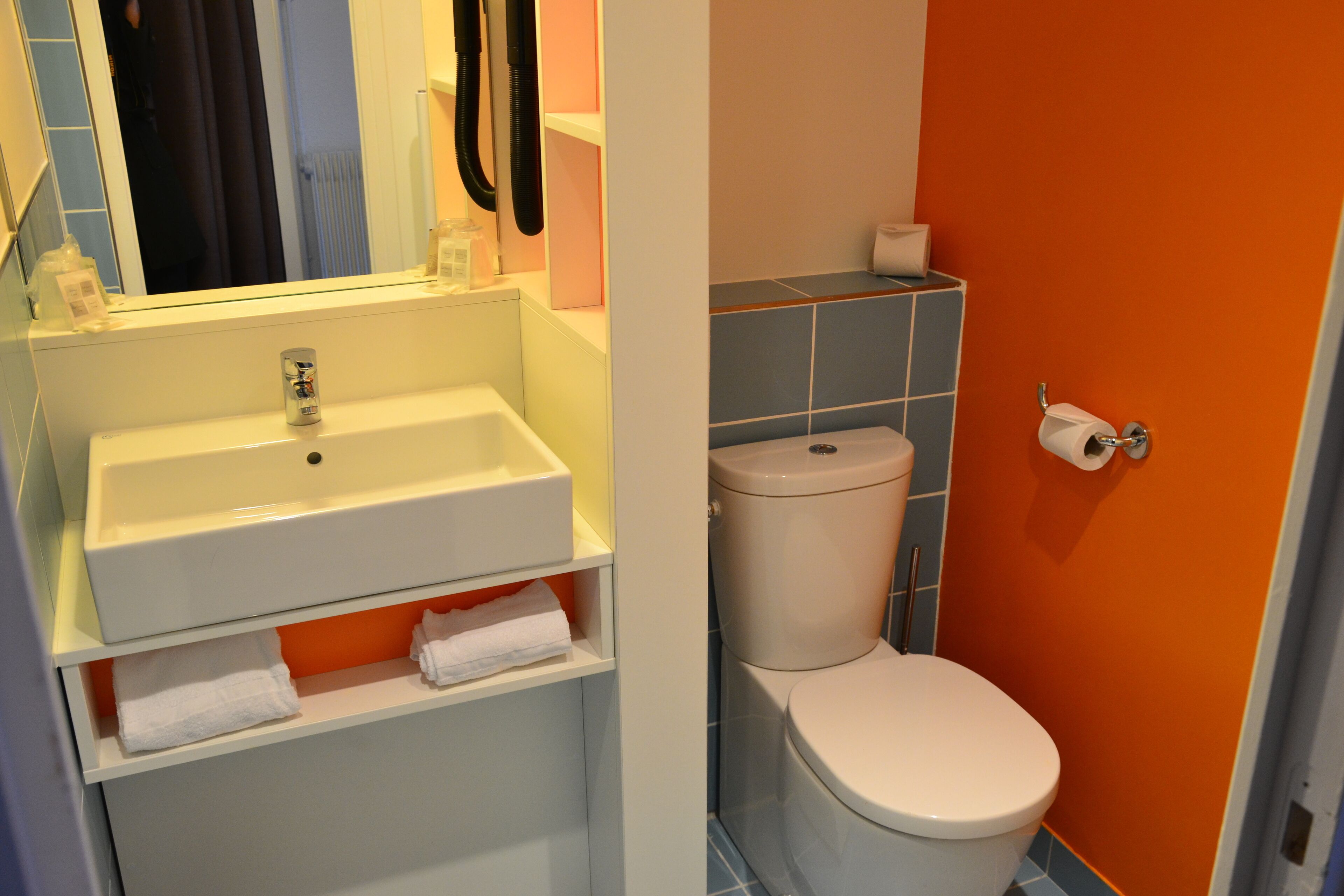 Une salle de bain avec un lavabo blanc, des toilettes et des murs orange.