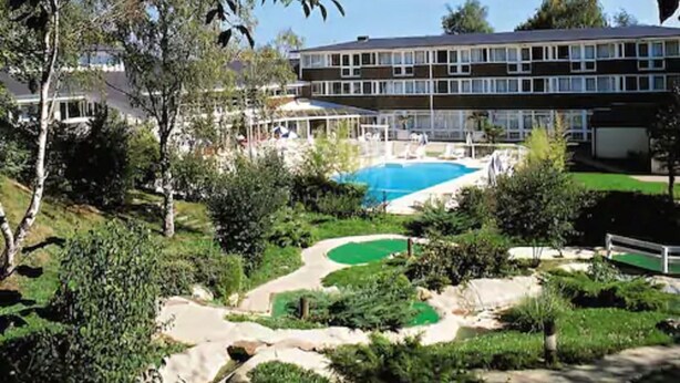 Un hotel con piscina, rodeado de vegetación y un campo de golf.