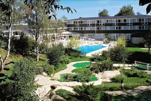 Un hotel con piscina, rodeado de vegetación y un campo de golf.