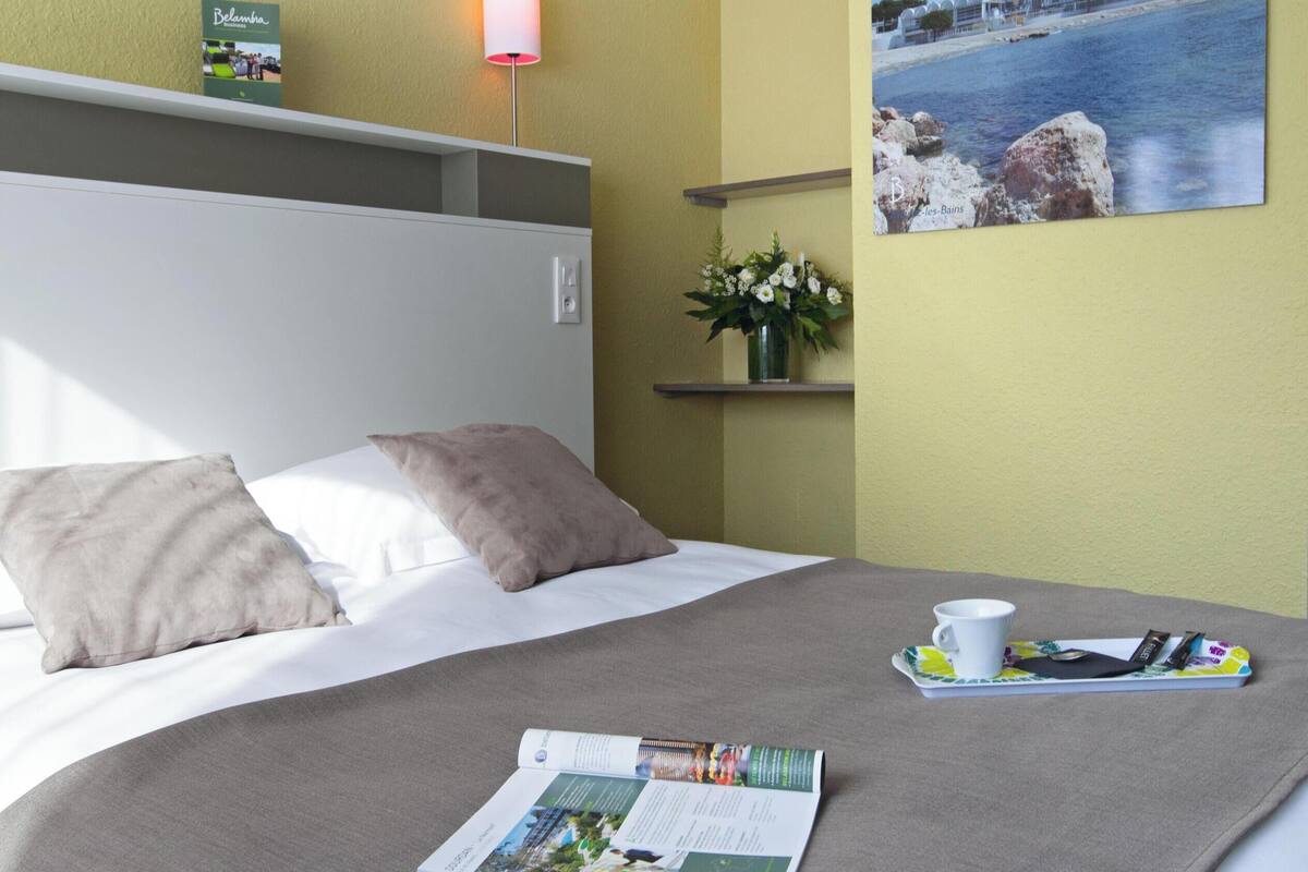 A neatly made bed with a magazine, a cup, and a smartphone on a tray.