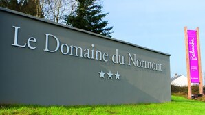 Señal de Le Domaine du Normont con tres estrellas y un edificio pequeño al fondo.