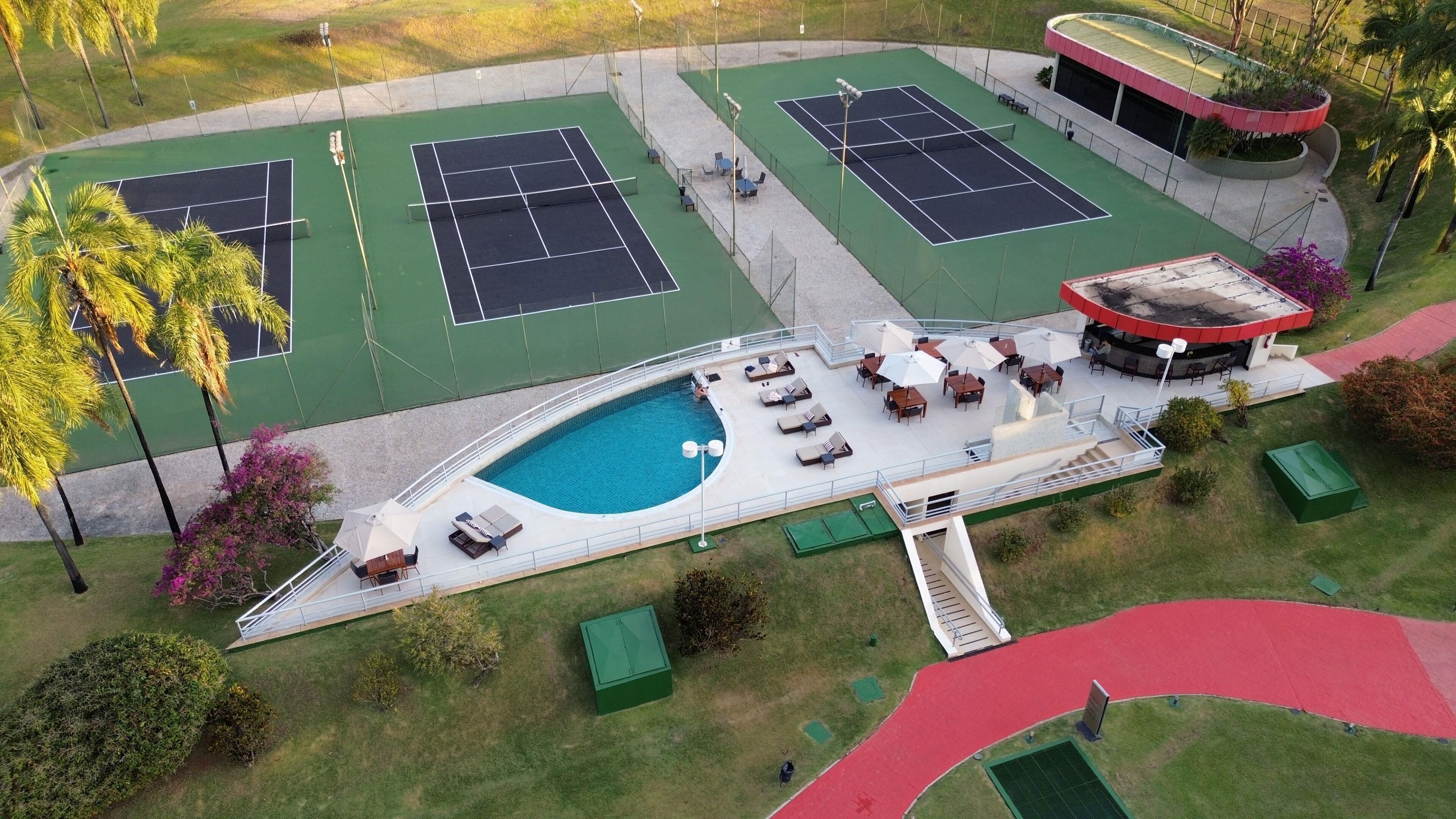 An aerial view of a tennis court complex with a swimming pool, outdoor seating, and a covered area.