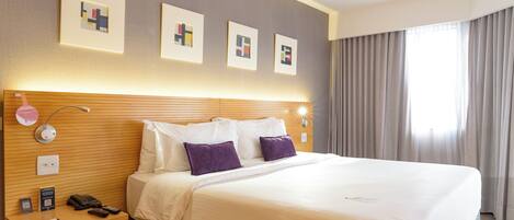 A hotel room with a large bed, a wooden headboard, a nightstand with a lamp, and artwork on the wall.