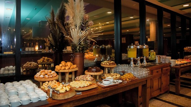 Ein reichhaltiges Buffet mit verschiedenen Speisen und Getränken, präsentiert auf einem Holztisch. Im Hintergrund ist ein großes Fenster zu sehen.