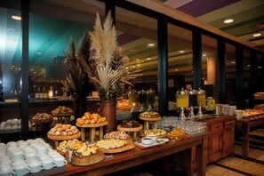 Ein reichhaltiges Buffet mit verschiedenen Speisen und Getränken, präsentiert auf einem Holztisch. Im Hintergrund ist ein großes Fenster zu sehen.