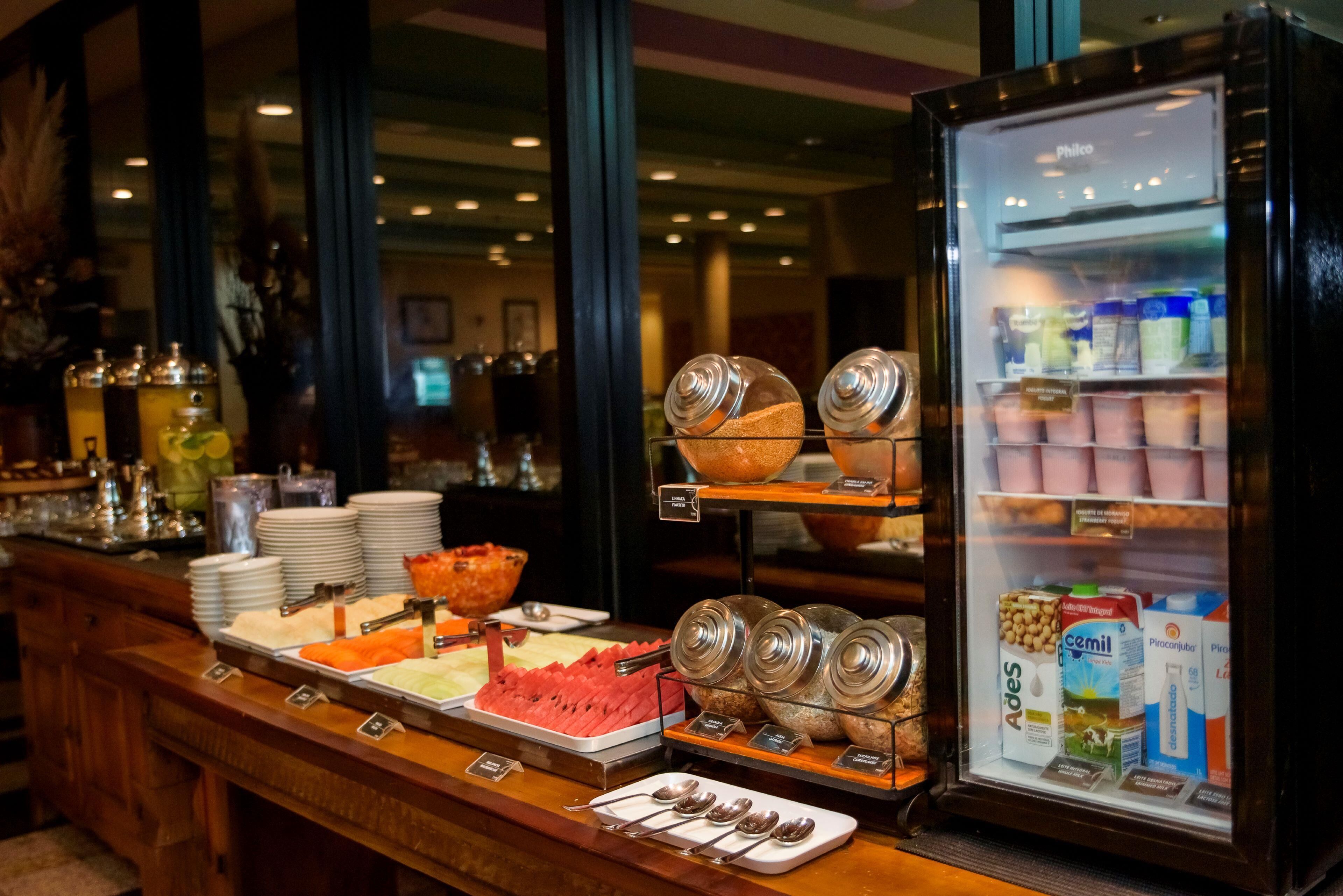 Un bufet amb diversos plats i condiments, una vitrina refrigerada plena de begudes, i una finestra amb vista a l'interior.