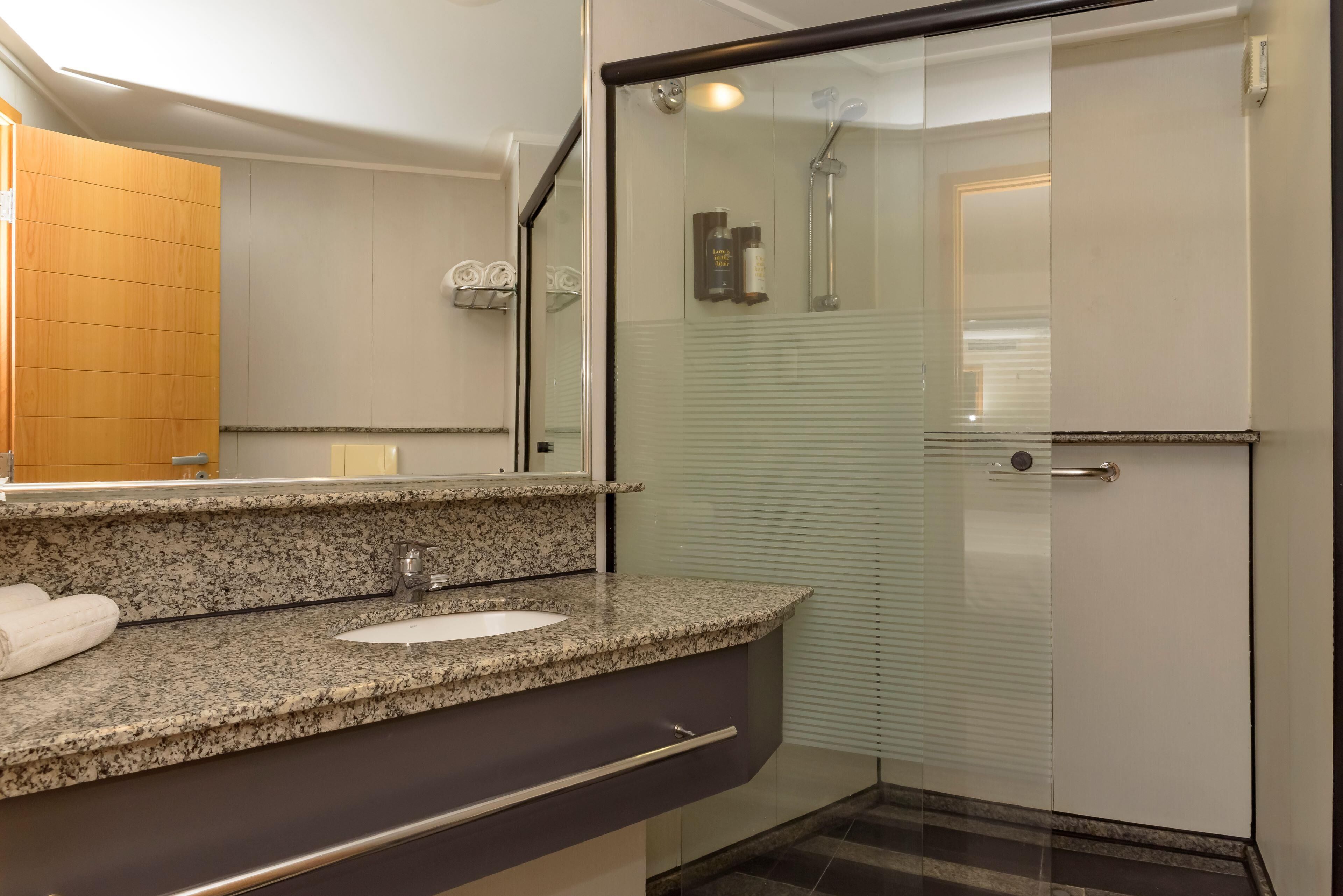 Un baño moderno con encimera de granito, un lavamanos blanco y una ducha con cerramiento de vidrio.