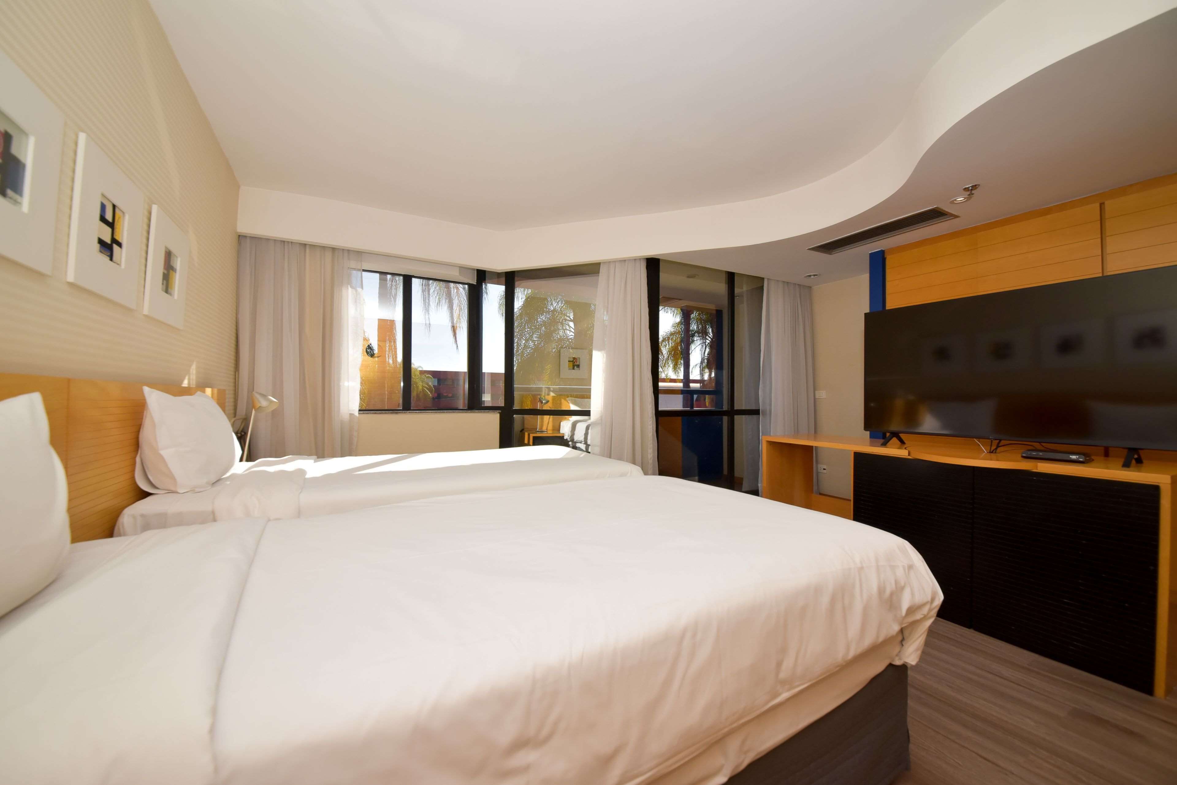 A hotel room with two beds, a TV, and a large window.