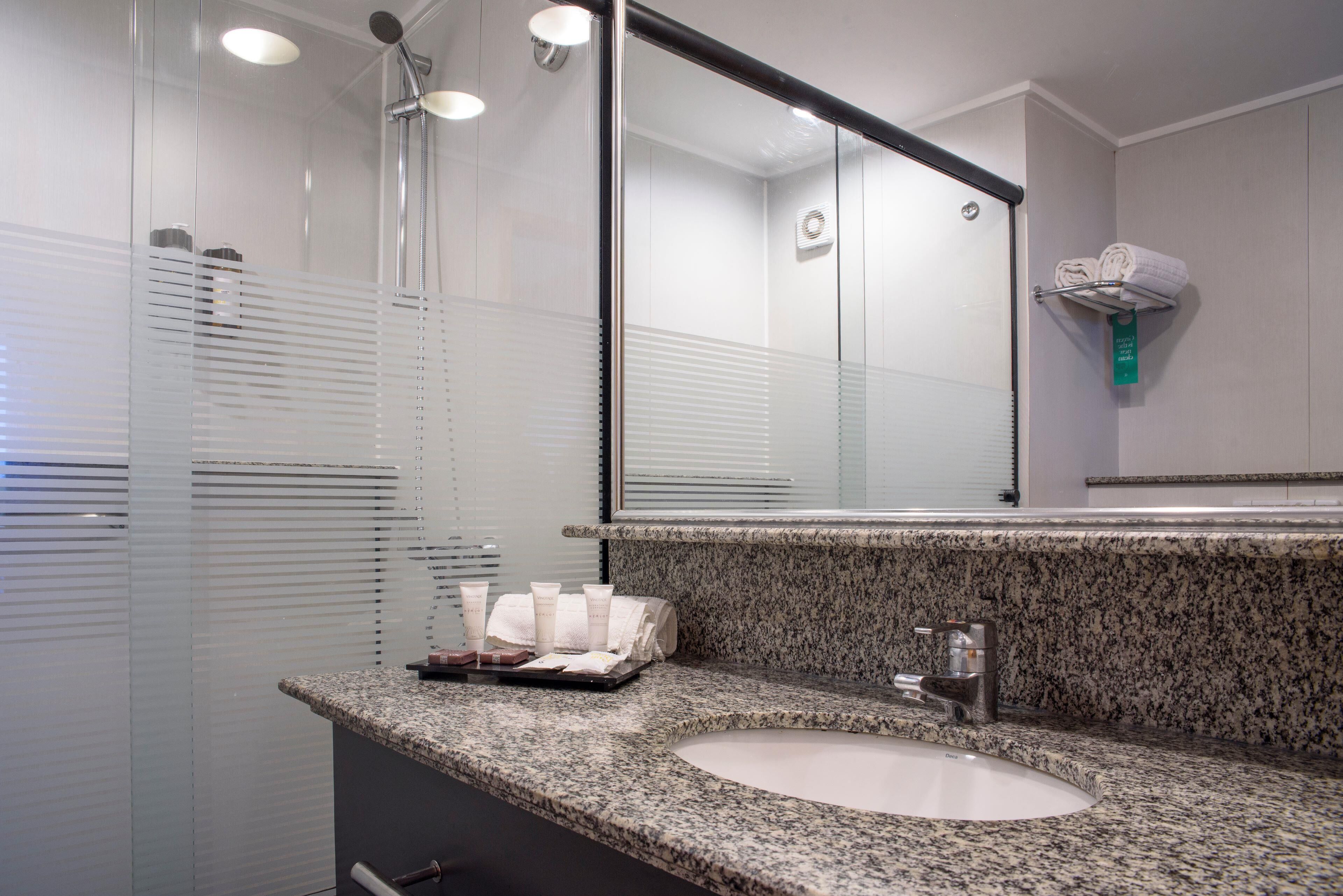 A modern bathroom with a granite countertop, a sink, a mirror, and a shower enclosure.